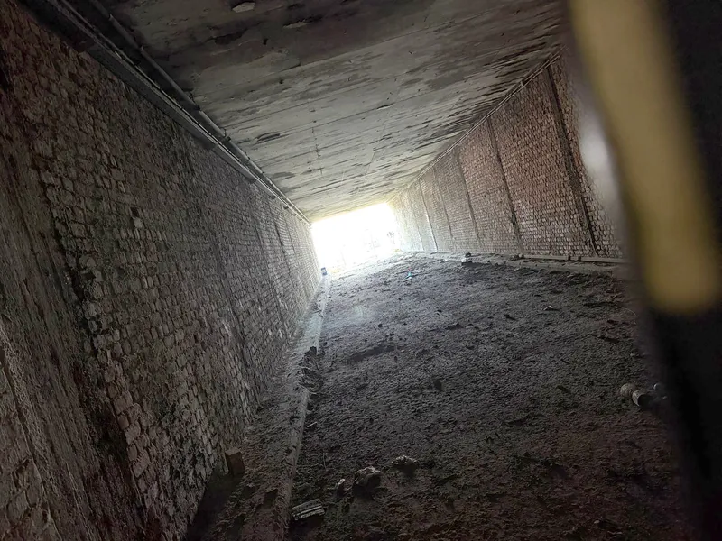 Donkere kelderdoorgang met bakstenen muren en een lichtopening aan het einde
